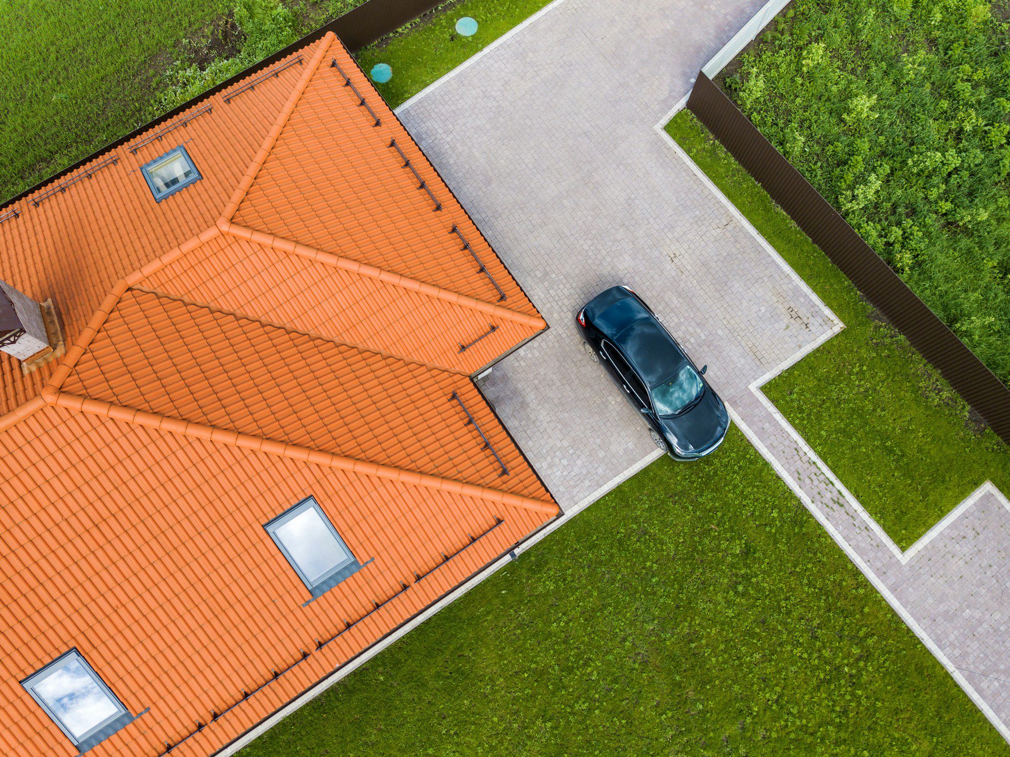 This is an aerial or top-down view of a building with a distinctive orange tiled roof. There's a car parked alongside the building on a paved area, and there are grassy areas surrounding the property. The architecture follows a symmetrical design, and it appears to be a residential area.